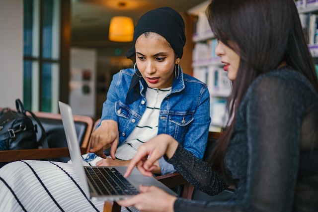 two-women-looking-and-pointing-at-macbook-laptop-1569076